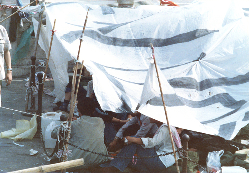 從這一張圖，可以看出學生的「帳篷」是怎麼搭起來的。用竹竿綁在原有的鐵欄杆，再綁上塑膠布、帆布，就是學生長住的帳篷，條件其實是非常簡陋的。雖然如此，卻勉強可以遮風避雨。